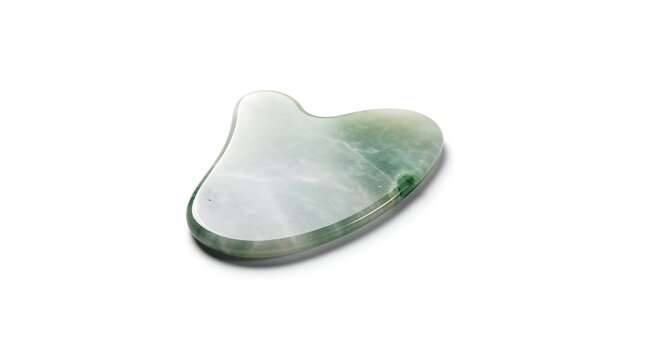 A smooth green jade gua sha stone rests against a clean white background.