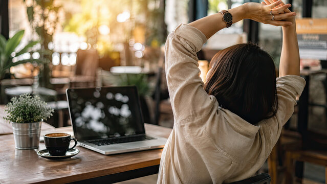 Remote work, Bangkok cafe. Close-up of a woman stretching arms above their head while seated at a cafe table with a laptop and coffee nearby. Work-life balance concept.