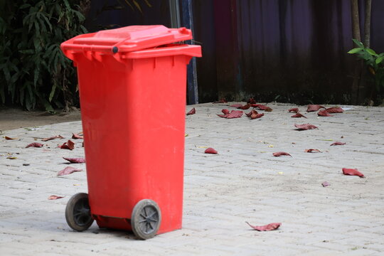 Trash bin surrounded by scattered fallen leaves in outdoor environment naturally