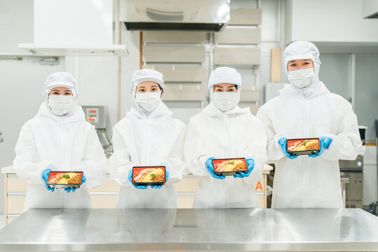 A man and a woman preparing bento boxes in a kitchen (food factory, food processing, food hygiene)