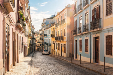 Fototapeta premium A sloped narrow cobblestone street lined with pastel-colored residential buildings in a European town on a sunny day.