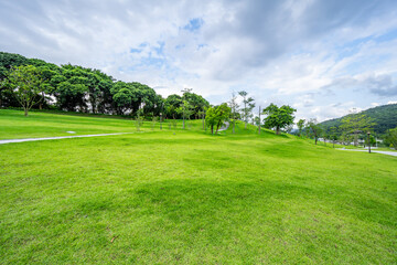Obraz premium An expansive, lush green lawn set against rolling distant mountains under a blue sky with white clouds.
