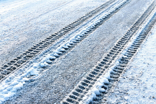 Clear tire tracks are left on a snow-covered roadway, showing vehicle paths in cold winter weather.