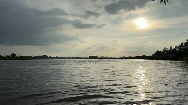 Dramatic sun shining over calm river water under cloudy sky. 4k video 60 fps