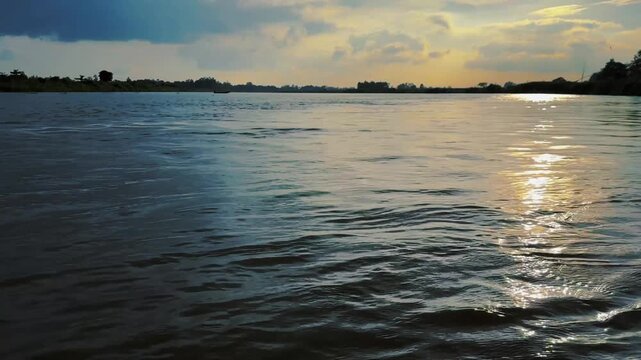 Golden sunset reflecting on wide river surface under dramatic clouds. 4k video 60 fps