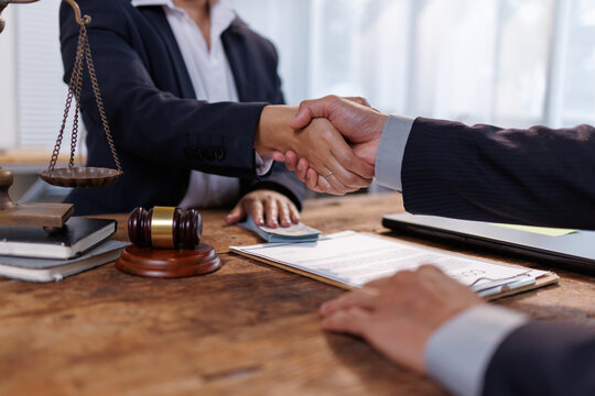 Lawyers or business partners shaking hands after reaching an agreement or closing a deal. With a contract. Money. Scales of justice. And a gavel on the table