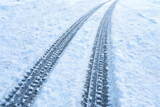 Two parallel tire tracks left in fresh white snow, extending along a rural winter path, showing vehicle travel on snowy terrain.