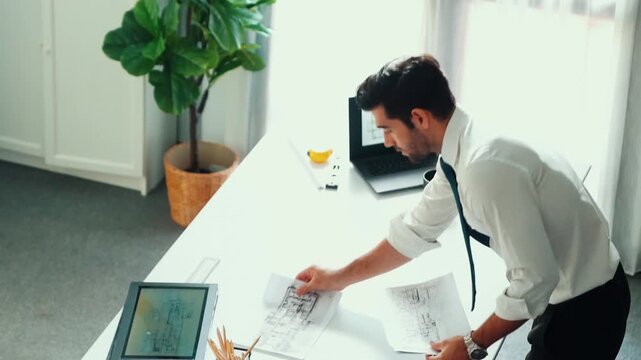 Architect engineer using laptop planning house design at office while sitting at meeting table with blueprint and equipment scatter around.Skilled civil engineer working at blueprint. Alimentation.