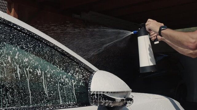 Car wash. Car in washing process. Carwash station. Washing car in workshop. Professional work. Car washer doing manual foam washing in auto detailing service. Hand washing with foam and spraying
