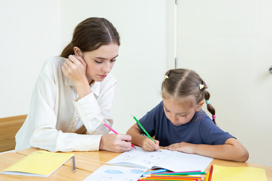 Teacher assisting young student with drawing and learning activity in classroom. Creative education, child development, personalized learning, and academic support concept.