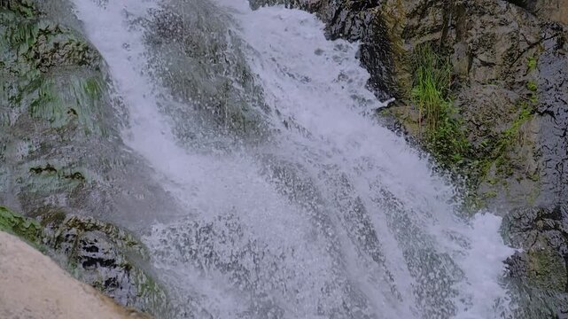 Slow motion: waterfall in the mountain - river or stream of water is flowing and falling down - close up view. Nature, landscape and environment concept