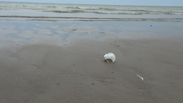Discarded plastic container polluting sandy beach near ocean waves