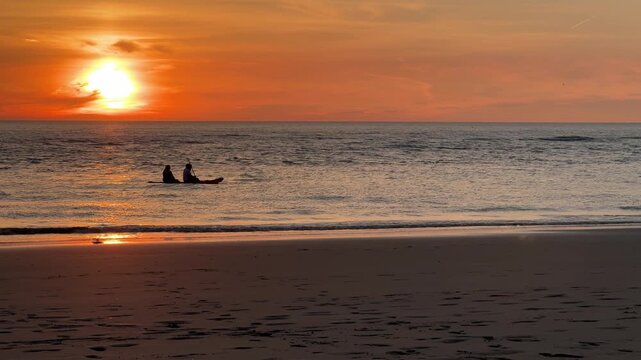 Two people paddling canoe across ocean at orange sunset