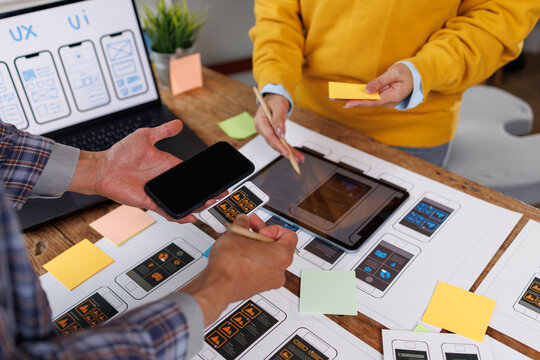 Design team collaborating on user interface and user experience - uiux - for mobile application development, prototyping new app layouts and wireframes on paper, tablet, and laptop