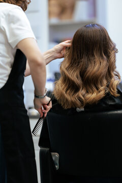 Professional Hairdresser Styling Client Curls With Wide Tooth Comb. Stylist uses narrow handle detangling tool arranging fresh wavy hairstyle for customer