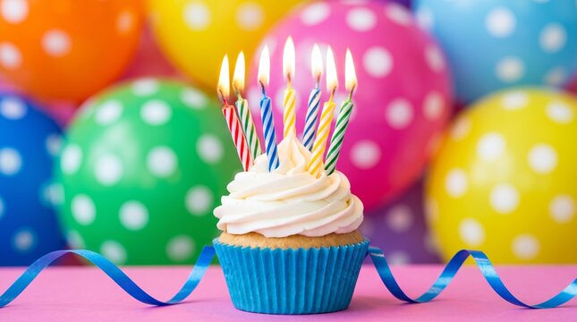 Lit birthday cupcake surrounded by vibrant polka dot balloons and blue curling ribbon decorations with against backdrop colorful cupcake topped swirling