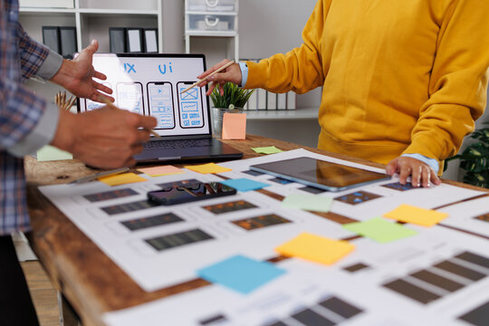 Collaborating on a new uiux design, two people review mobile app mockups on a laptop and discuss wireframes