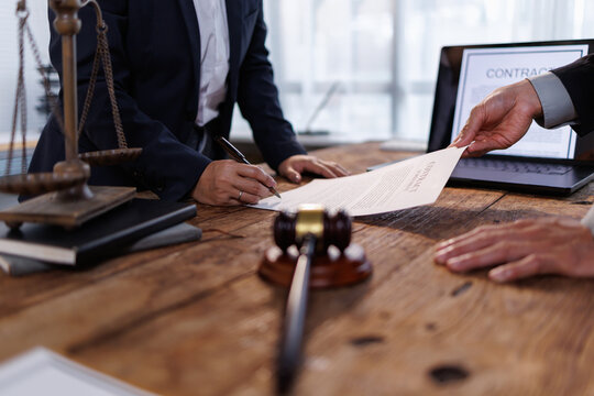 Lawyer or client signing legal contract documents at a wooden desk with a judge's gavel and scales of justice, symbolizing business agreement and legal counsel