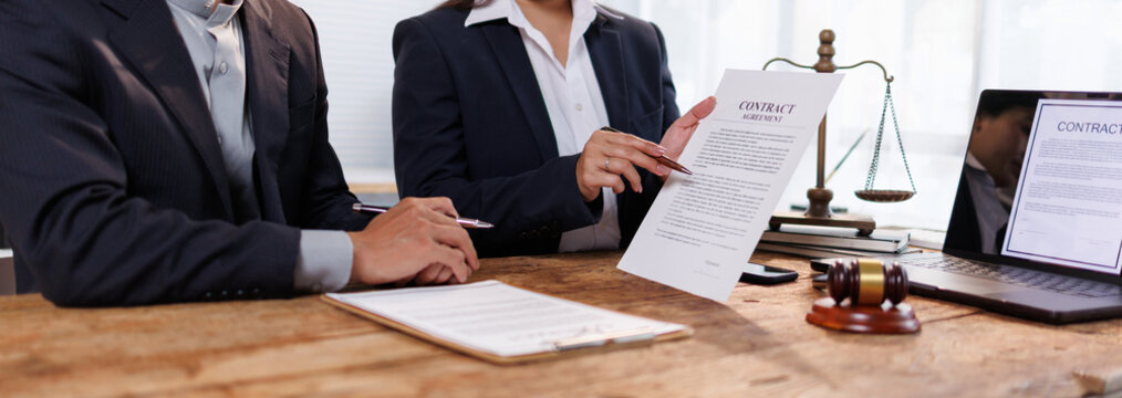 Lawyers discussing contract agreement terms with a client, providing legal advice and negotiating business law details in a professional office setting