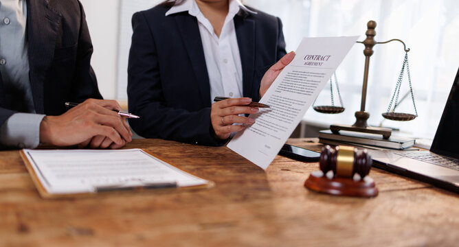 Legal professional consulting client on contract terms, explaining clauses and discussing agreement details during a meeting, with scales of justice and gavel on wooden desk