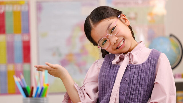 Cheerful Young Schoolgirl in Pink Glasses Posing in a Colorful Classroom
