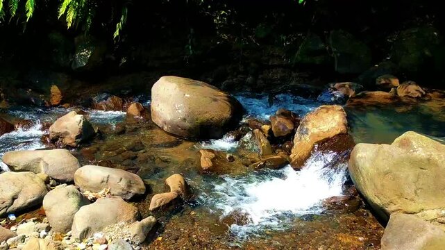 A river carries a slow, steady current through a rocky landscape, water forming small eddies along the edges of stones. 