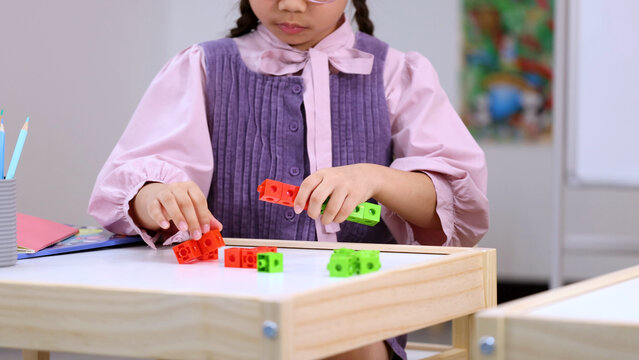 Young Schoolgirl Connecting Colorful Plastic Learning Blocks at a Classroom Desk