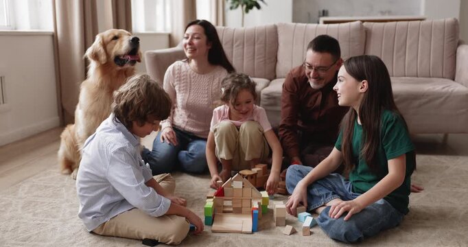 Large family spending time together on floor in living room, children playing with wooden blocks, communicate with loving parents and golden retriever dog at home. Bonding, leisure activity indoors