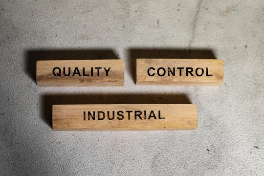 Top view of wooden blocks displaying the words quality, control, and industrial on a concrete background. Industrial quality assurance concept for manufacturing, inspection, compliance, and production