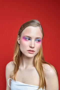 A woman with bright, expressive eye makeup on a red background. Her expression is serious, focused, and confident.