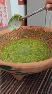 Stirring Green Guaje Salsa with Spoon in Clay Bowl