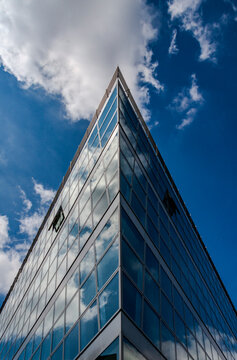 Close-up of the corner of a modern office building with a glass facade. Bright sunshine reflects white clouds in the windows, emphasizing clean architectural lines and contemporary design.