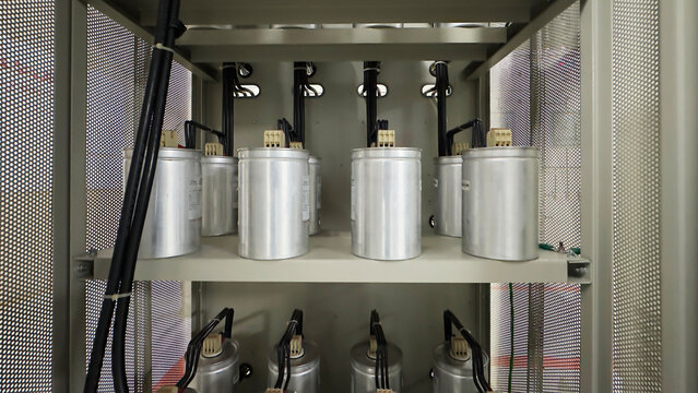 Row of industrial power factor capacitors inside electrical control panel cabinet with heavy wiring and cable connections.