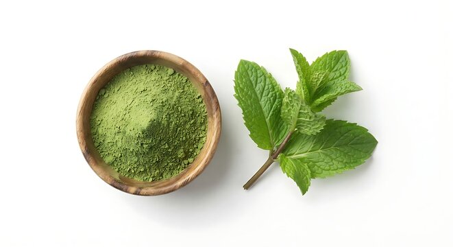Fresh mint leaves next to bowl filled with vibrant green mint powder on clean white surface