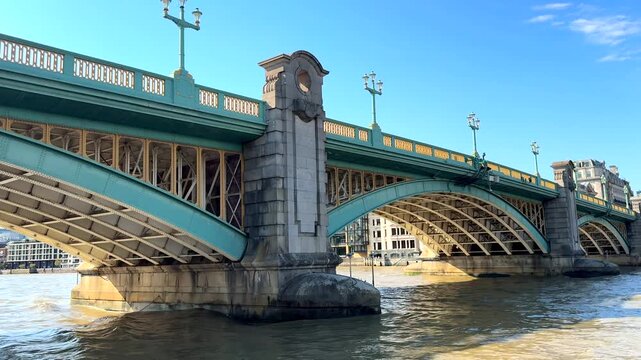 A steel arch bridge crosses a wide river with decorative stone piers and lamp posts