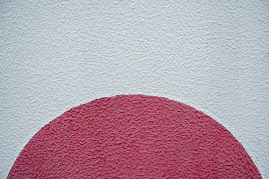 Red half circle shape painted on a rough white textured concrete wall background