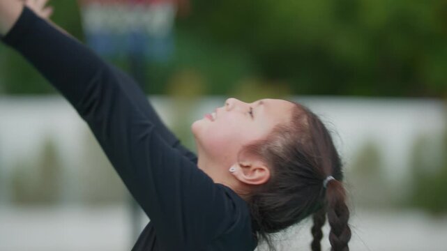 Young girl smiles while playing with a pink ball. Her long braid sways as she runs on a sports field. She wears a black outfit and appears joyful and active
