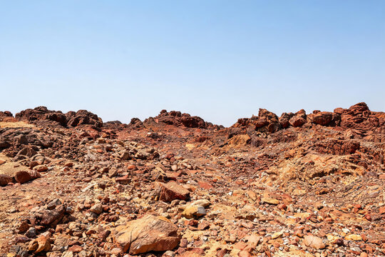 A barren rocky arid landscape under a clear cloudless sky, showing exposed geological formations.