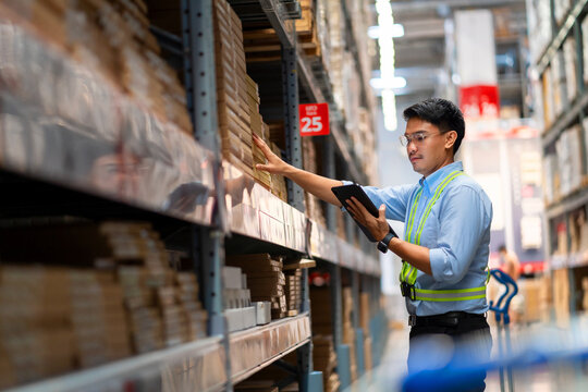 Warehouse worker in security uniform with tablet computer looking at merchandise in large warehouse Logistics and export business Logistics distribution center.