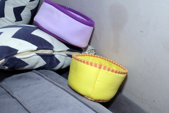 Two small colorful fabric storage containers placed on a couch next to a geometric patterned cushion.