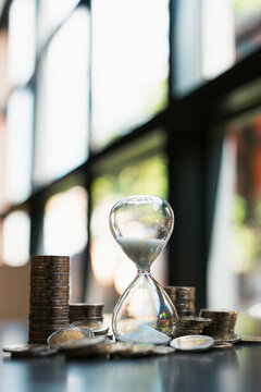 financial time management concept with hourglass standing among stacks of coins on table, representing investment growth, pension planning, time is money, tax deadline, and saving goals