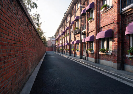 A narrow urban alley flanked by red brick buildings with purple awnings, paved with asphalt and stone sidewalks.