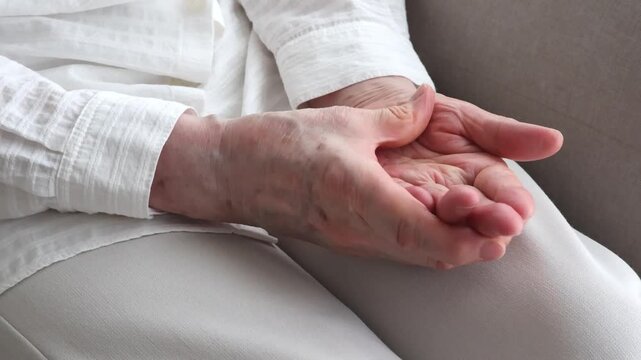 An elderly woman massaging her hands on her lap.