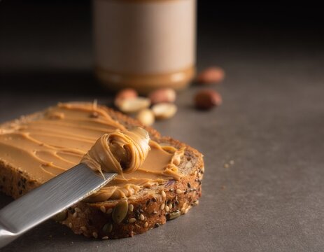 Knife spreading peanut butter on multigrain bread. Dark moody background with a blurred jar and loose nuts. Appetizing and warm food photography.