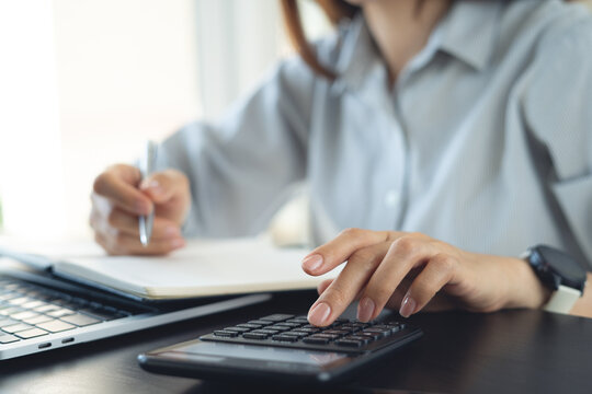 Doing finance, budgeting and tax calculation concept. Woman using calculator to calculate financial report at office desk, accounting with laptop, budget management