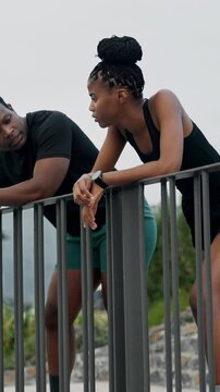 Fitness, couple and talking in city with rest, wellness tips and sports feedback for health. Runners, black man and woman outdoor on break, exercise conversation and chat with partner for story
