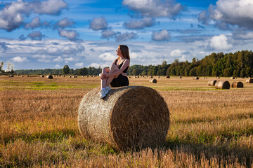 Girl Seated on Hay Bale Enjoys Late Afternoon Sun in Field © Aleksandr