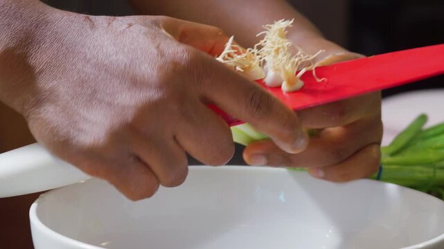 Trimming fresh green onion roots with red kitchen knife