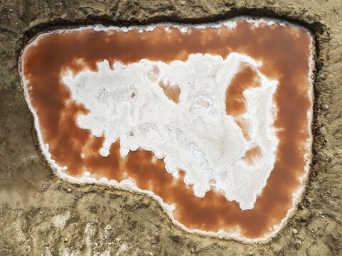 Saline pond with ruddy algae growth and white salt deposits at the Skeleton Coast. Aerial view. Drone shot. Namib Desert, Dorob National Park, Namibia