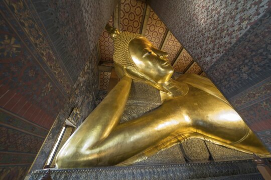 The monumental reclining Buddha shows the moment of entry into Nirvana. Golden surfaces, delicate patterns and warm temple colors accentuate the spiritual peace of this iconic depiction, Wat Pho, Bangkok, Thailand